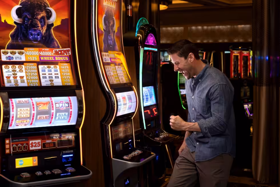 A person celebrates while playing a slot machine inside a casino. The machine displays winning combinations and jackpot amounts.