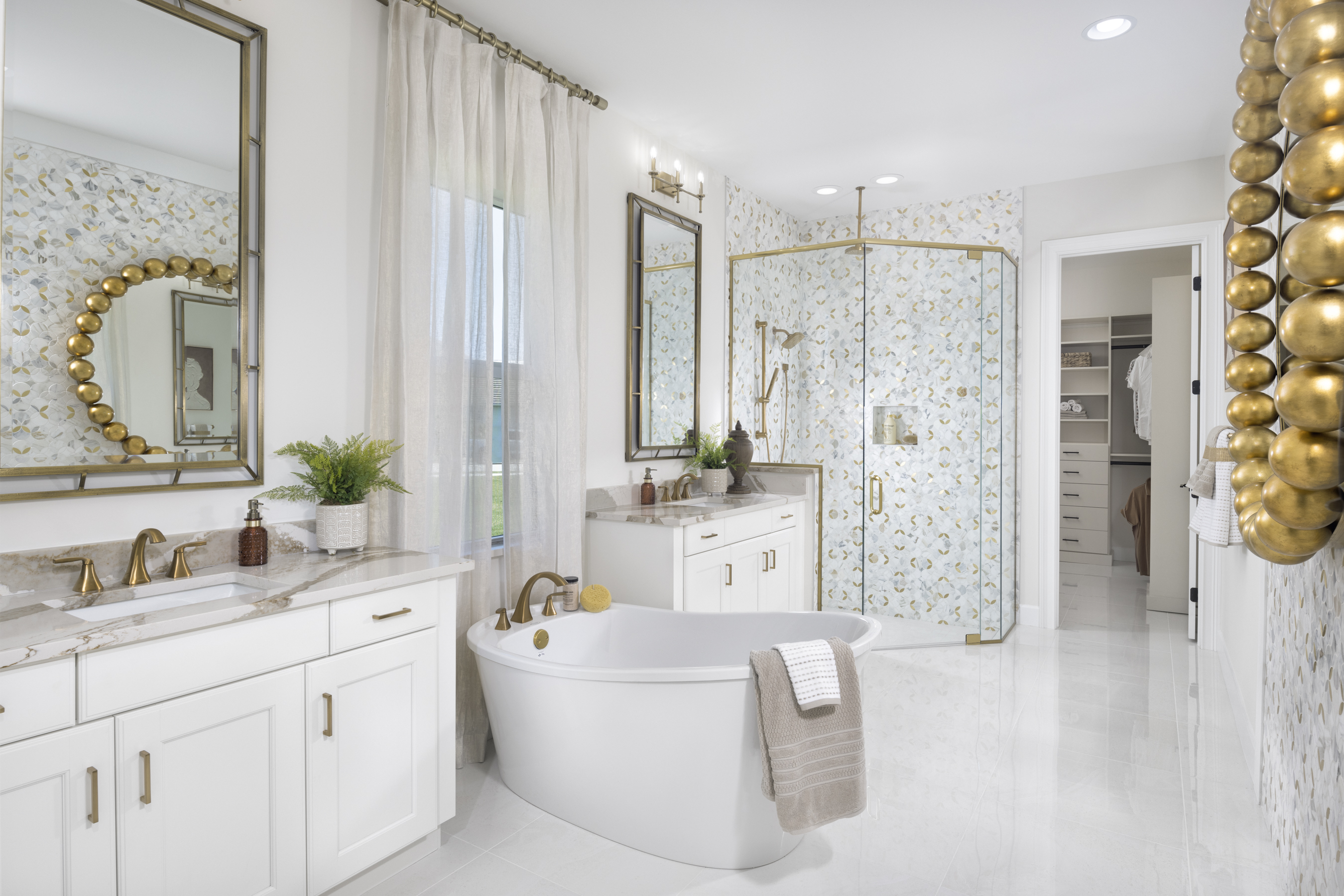 Elegant bathroom features a freestanding tub, marble countertops, gold accents, and a glass shower. Light, airy ambiance with decorative elements and plants.