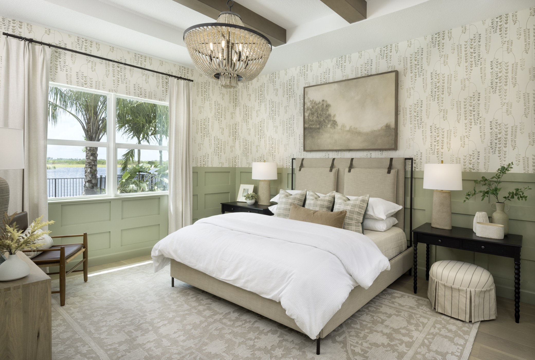 A cozy bedroom with elegant decor featuring a large bed, patterned wallpaper, and a scenic window view of palm trees by water.