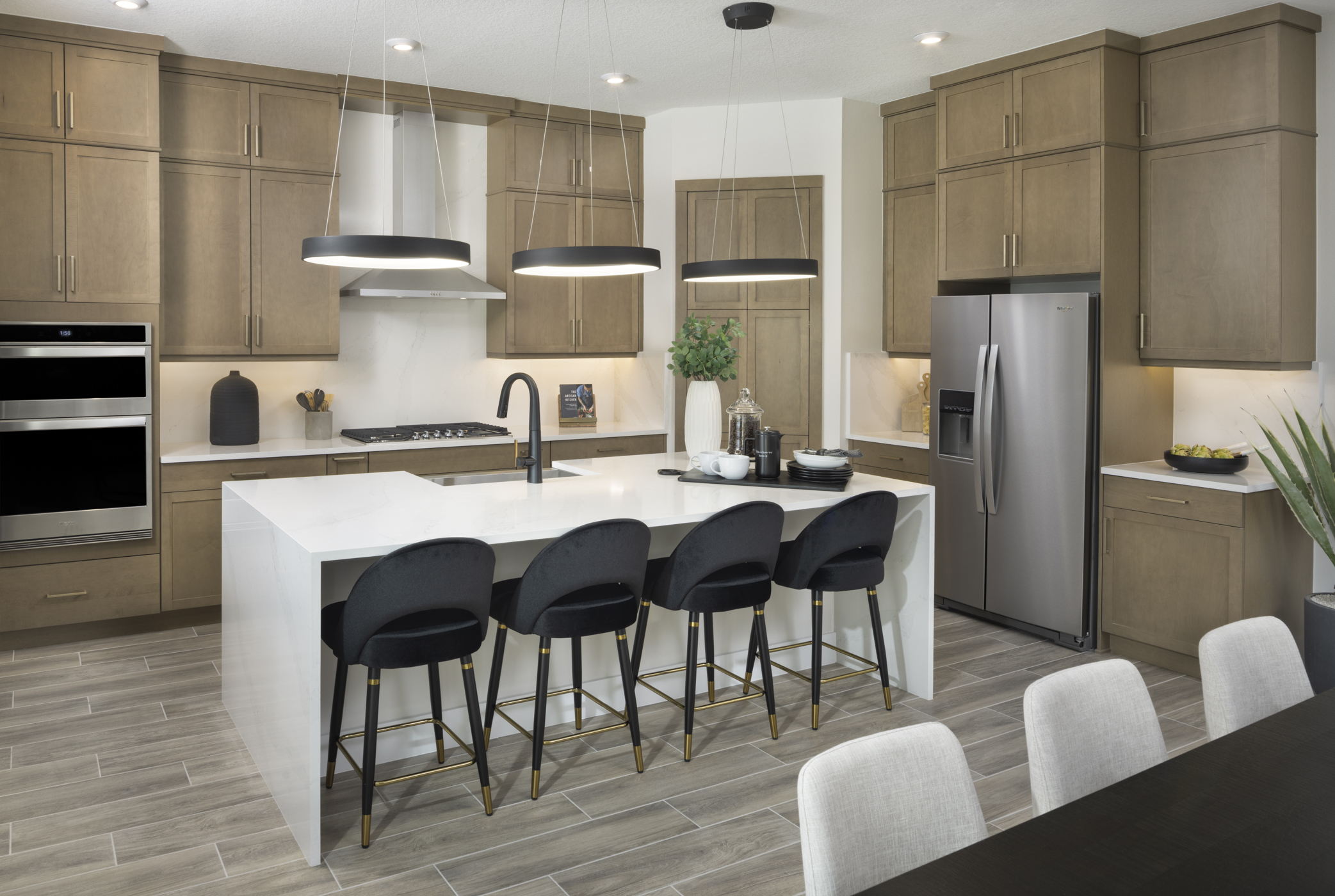 Modern kitchen with wooden cabinets, white countertops, black chairs, stainless steel appliances, pendant lighting, and decorative plants. Spacious, sleek design with elegant finishes.
